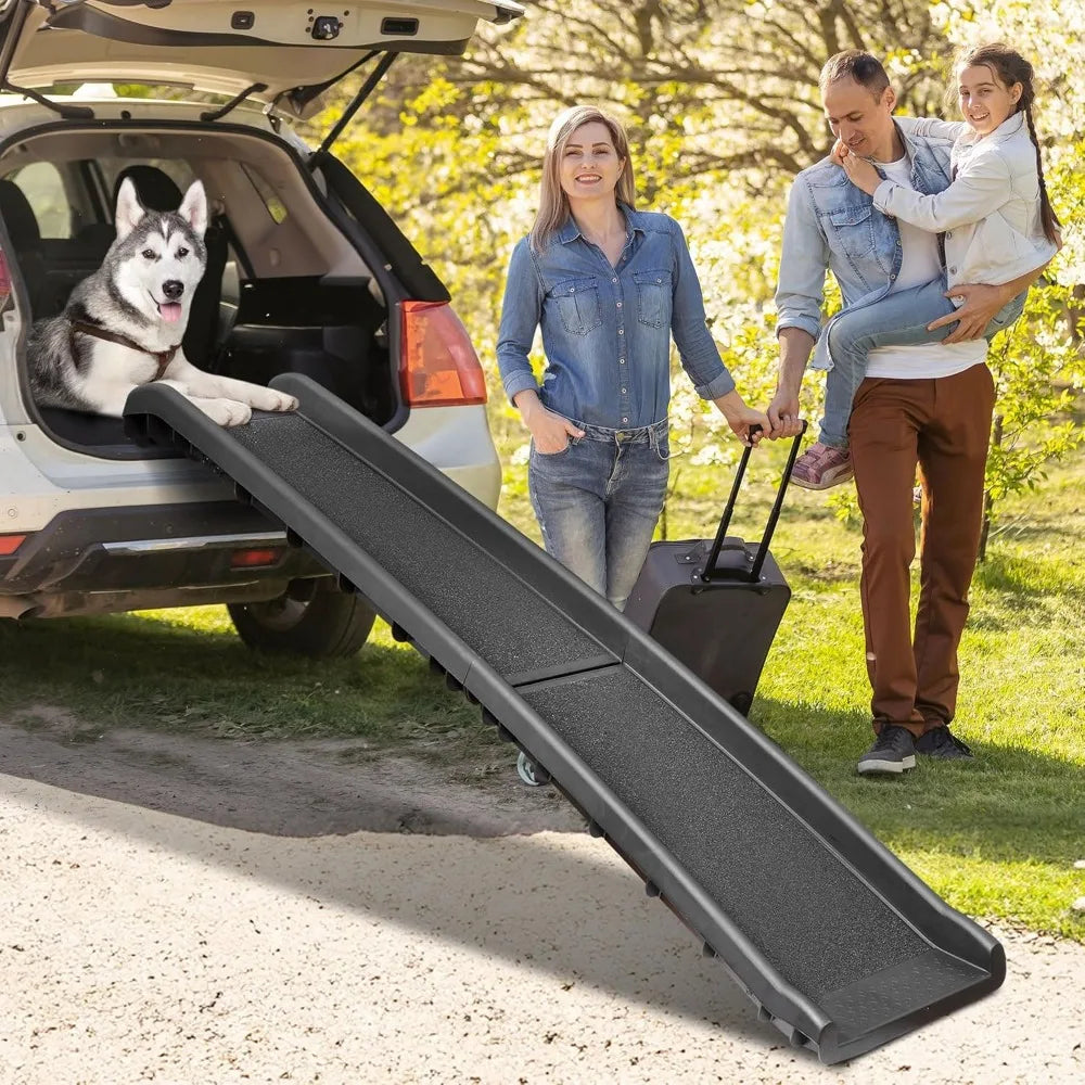 Folding dog ramp with raised siderails leading from grass up to the boot of a white SUV, husky waiting at the top