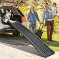Folding dog ramp with raised siderails leading from grass up to the boot of a white SUV, husky waiting at the top